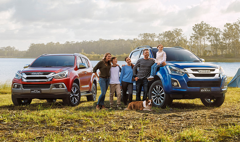 Family standing next to their Isuzu D-MAX and MU-X vehicles