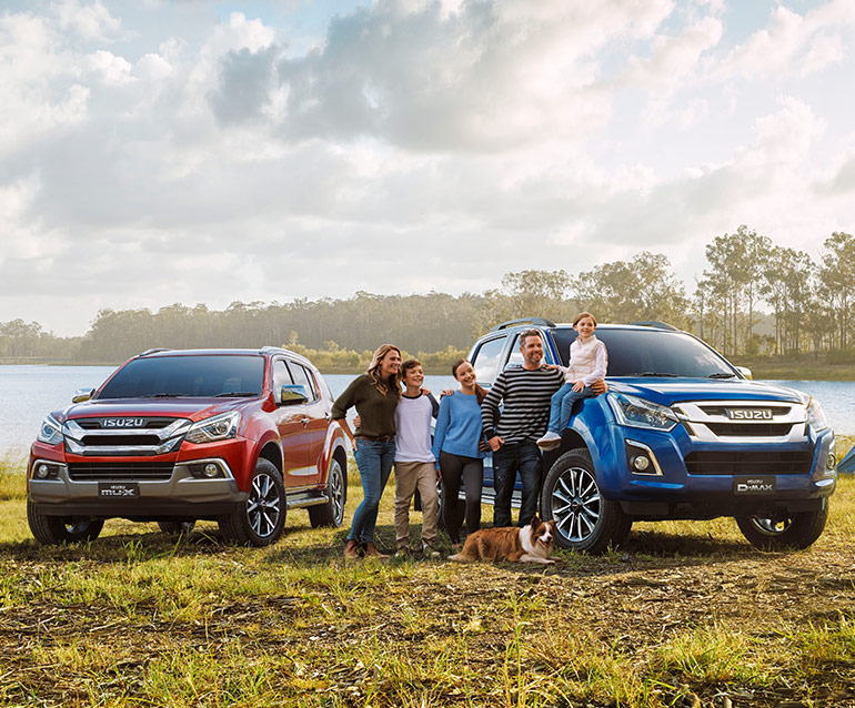 Family standing next to their Isuzu D-MAX and MU-X vehicles